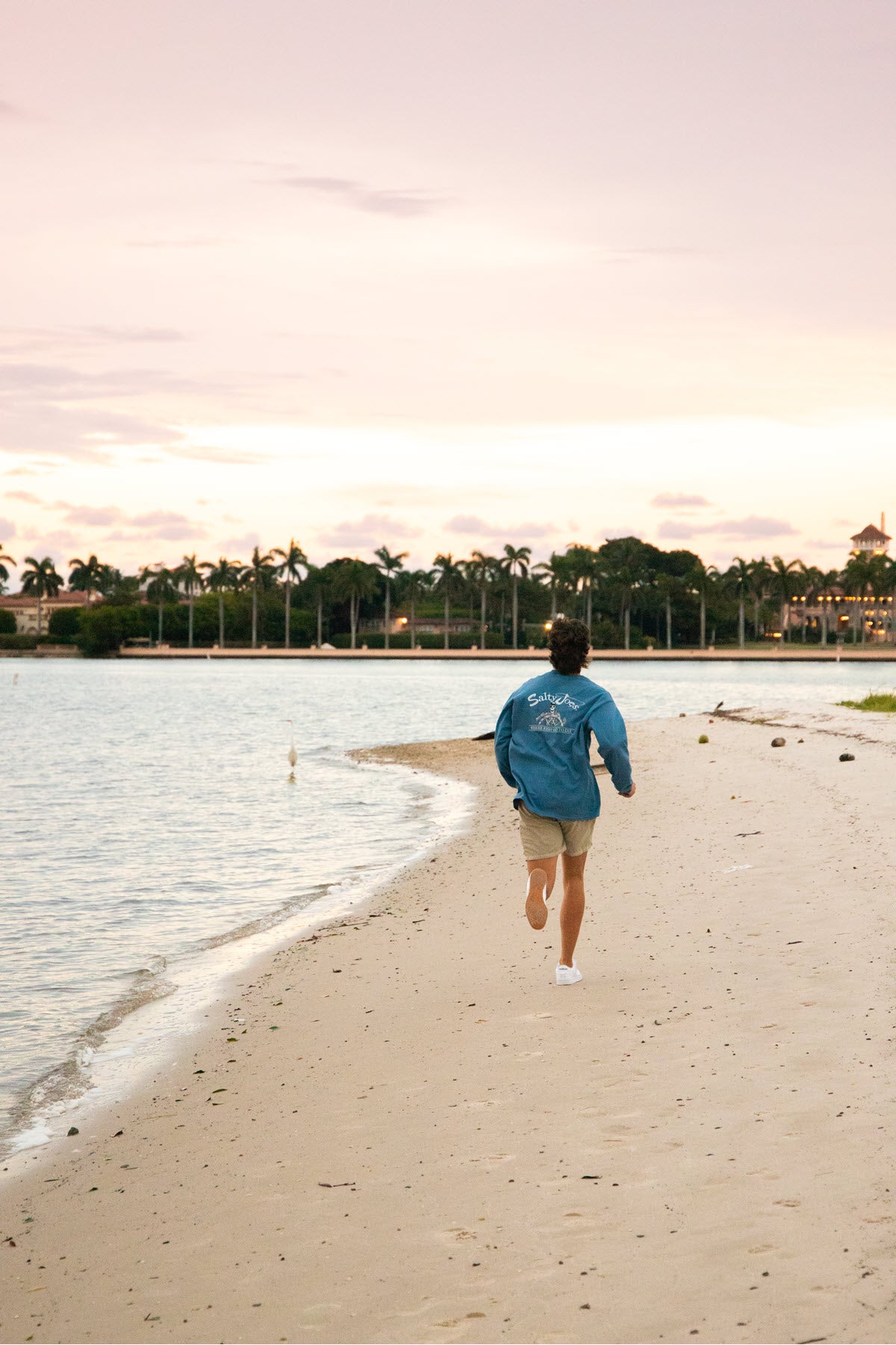 A man running on the beach in his fishing t shirt.